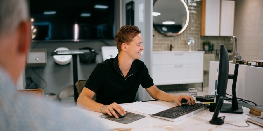 Nieuwe badkamer in Dalfsen nodig? Wij staan voor u klaar Medewerker van Tegelhome & HV Wonen helpt een klant aan zijn bureau.