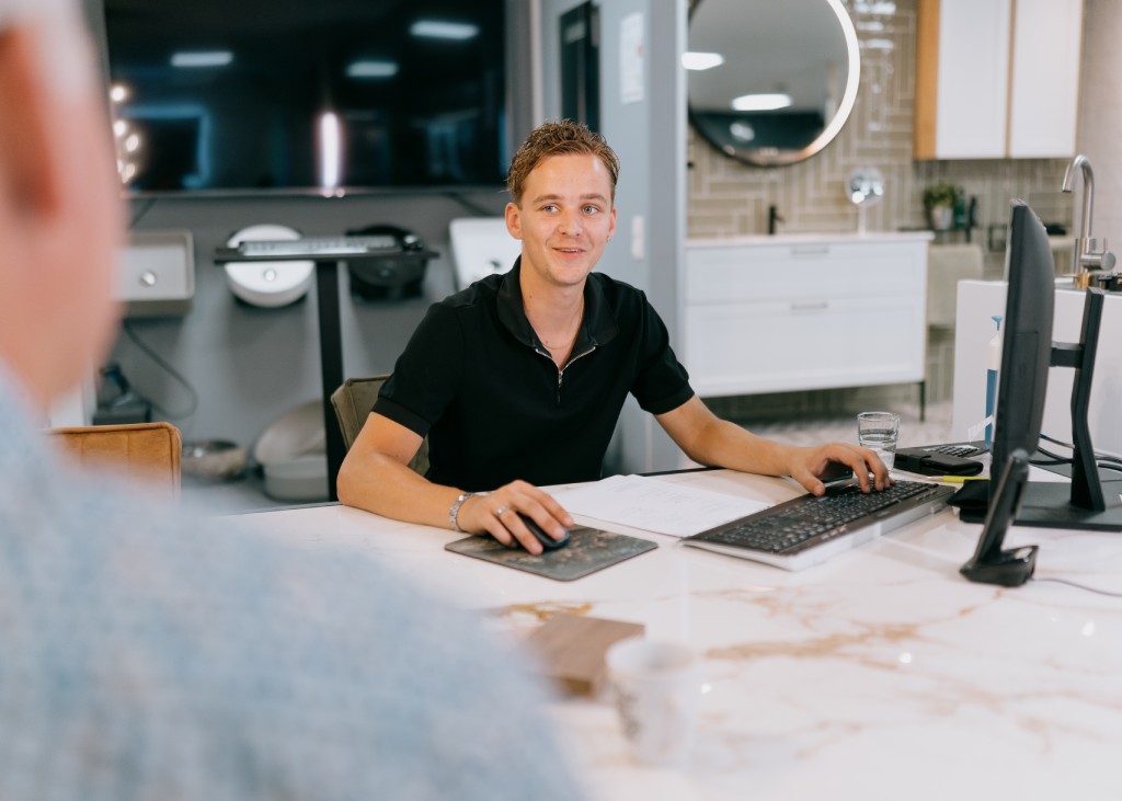 Gebruik maken van de voordelen van een badkamer inclusief montage in Zuidwolde? Kies voor Tegelhome. Medewerker achter de pc aan een bureau in overleg met een klant.
