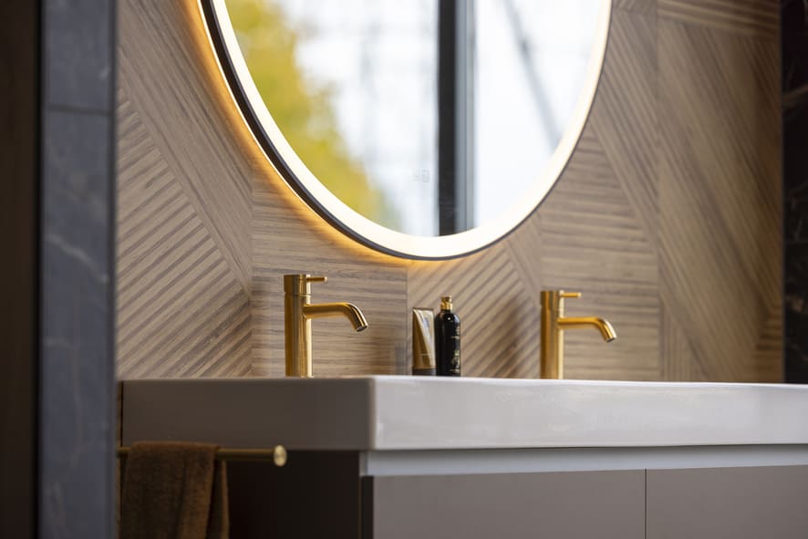 Moderne wastafel met gouden kranen en ronde spiegel in sanitair showroom in Zwolle