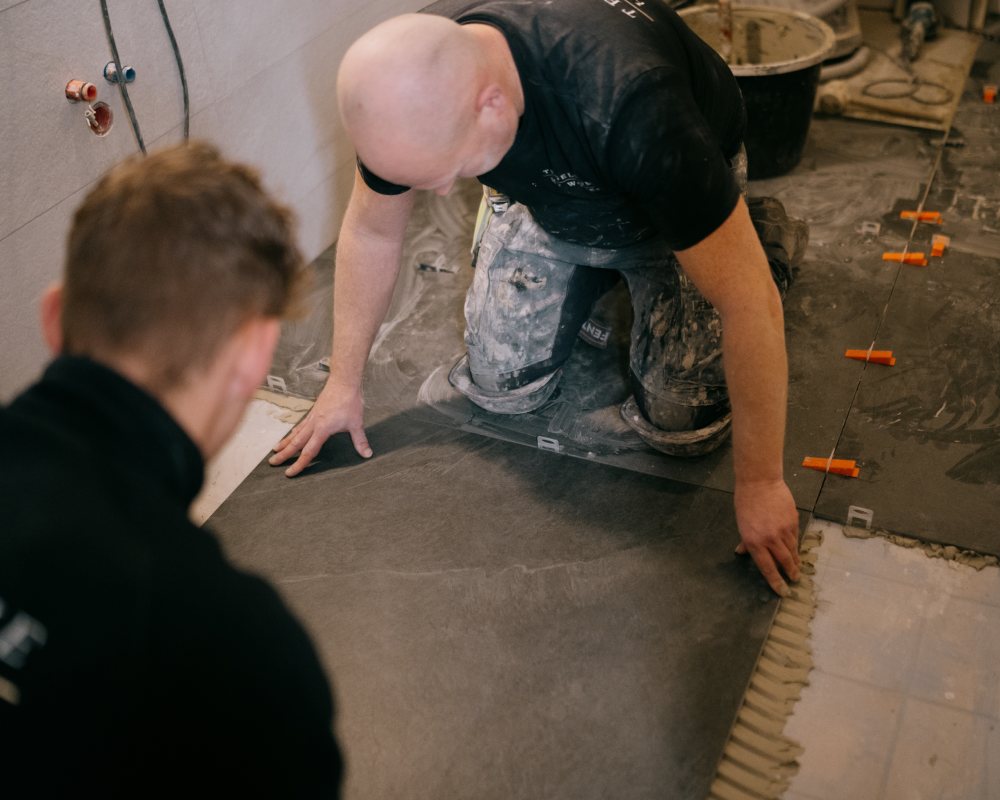 Vloer inclusief vloerverwarming leggen in Meppel. Twee medewerkers van Tegelhome leggen samen een tegel neer in de badkamer
